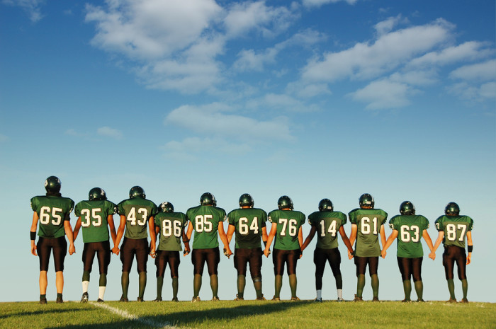 Football players holding hands against a blue sky