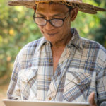 Old man with glasses and hat holding a tablet